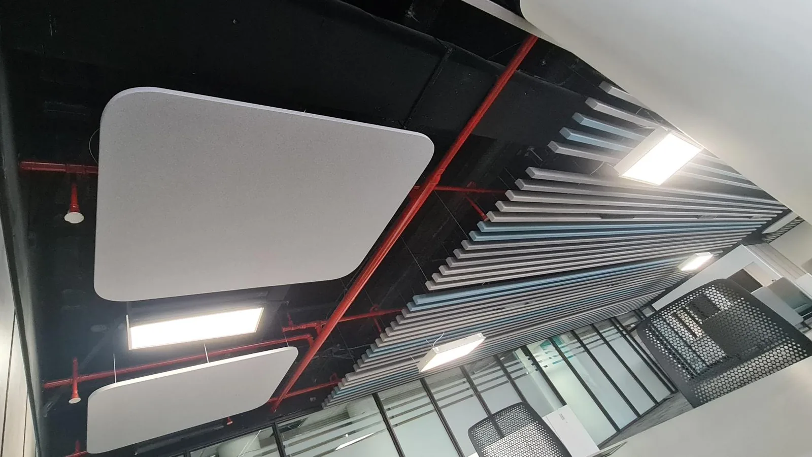 Acoustic cloud panels suspended below an open, black-painted soffit beside a baffle ceiling