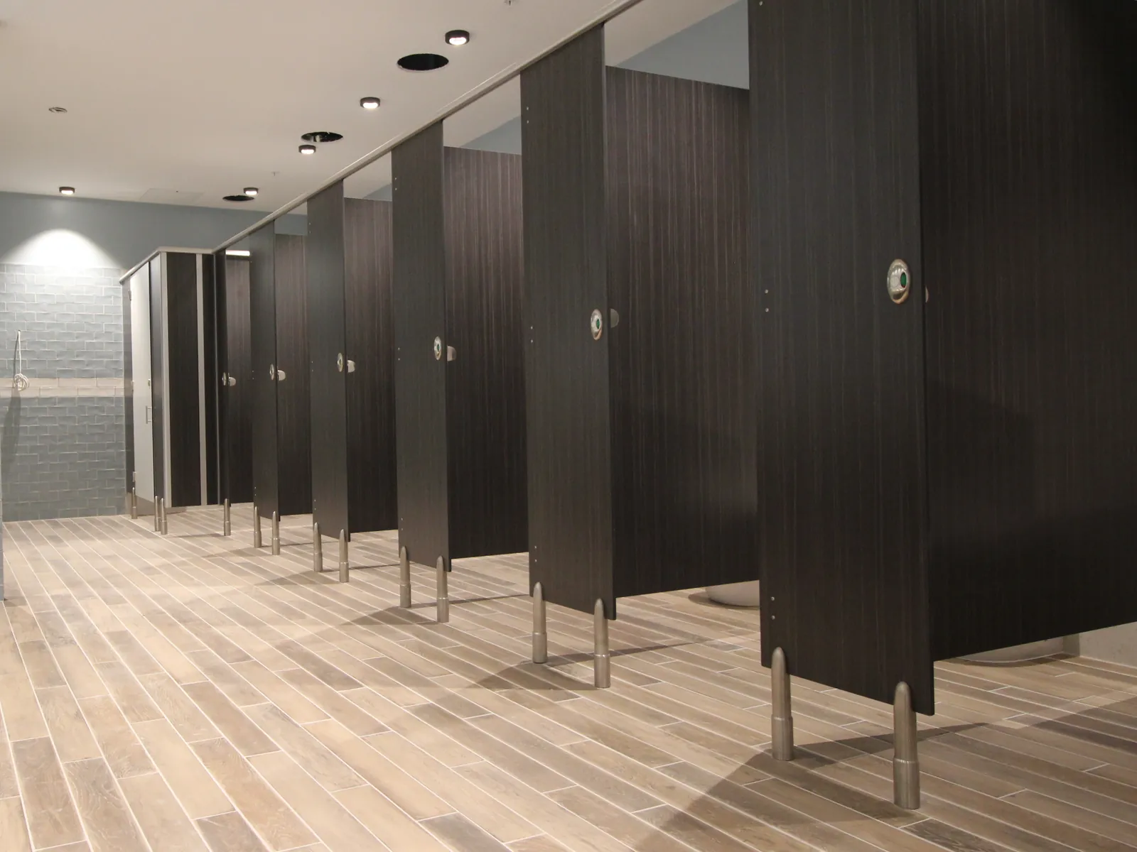 Dark toilet cubicles on metal adjustable legs in a tiled washroom with a washbasin counter